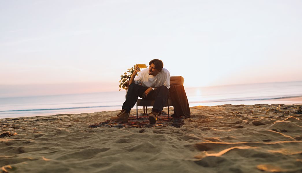 Langa dans un fauteuil sur la plage, l’abat-jour de la lampe à la main, au coucher du soleil