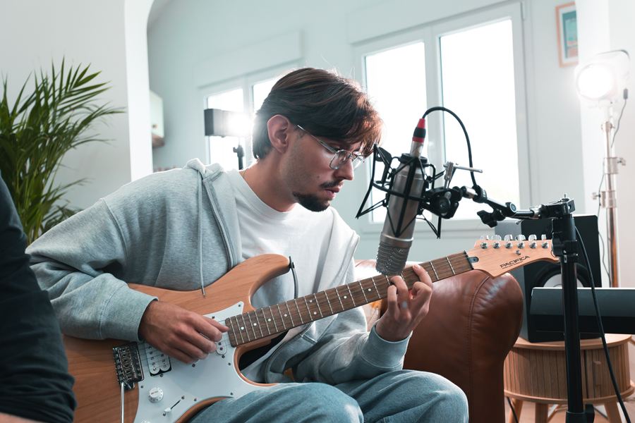 Langa joue de la guitare électrique devant le micro, dans la lumière des fenêtres