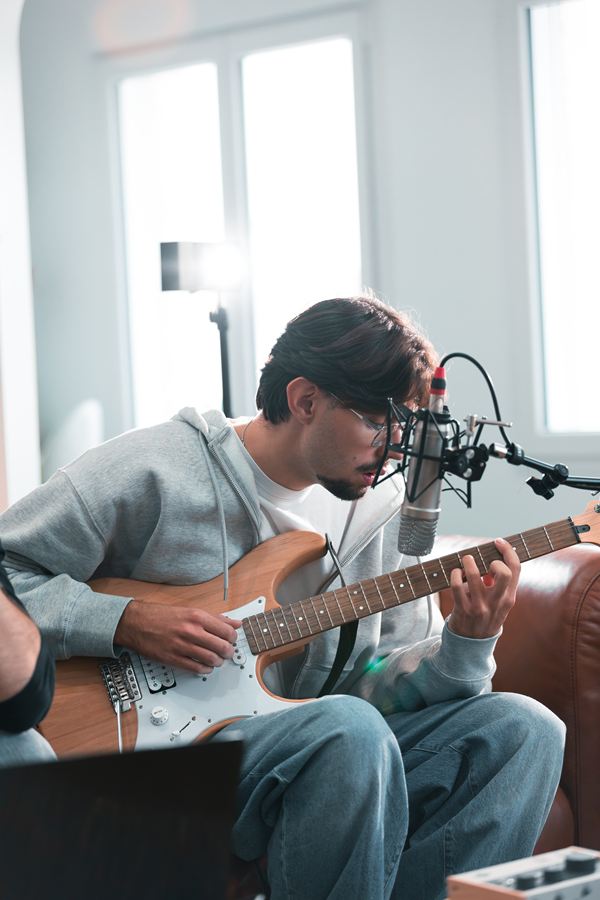 Langa chante au micro en jouant de la guitare électrique, dans un salon lumineux